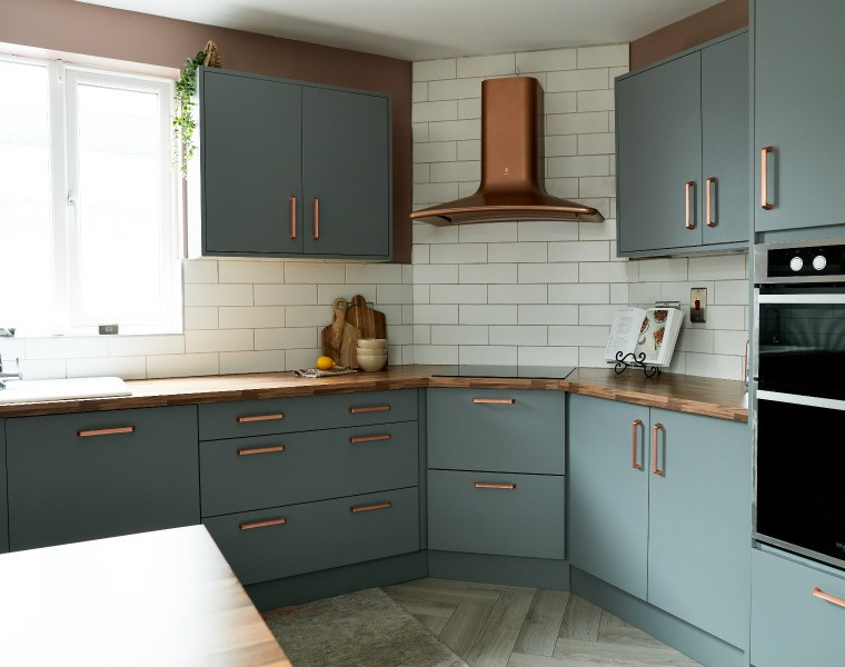 Corner of a Modica Dust Grey kitchen - flat, one-piece door with copper handles and extractor hood
